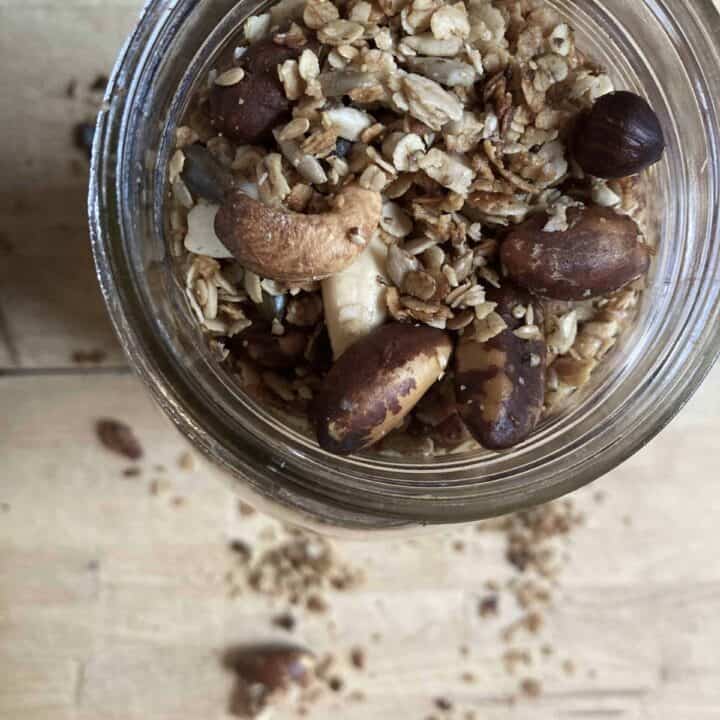 Homemade high protein granola in a glass jar on a wooden cutting board