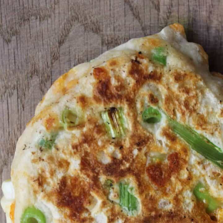 A sourdough scallion pancake with cheddar cheese and scallions on a wooden countertop.