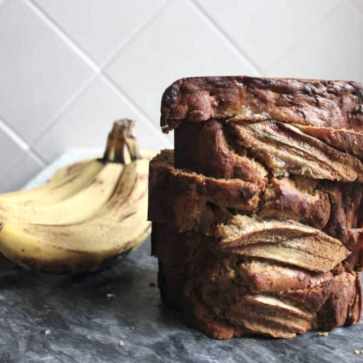 A photo of sliced sourdough discard banana bread against a white wall with bananas in the background.