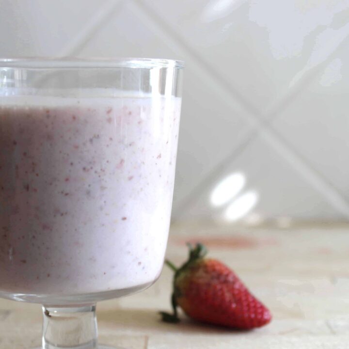 A strawberry kefir smoothie in a glass on a wooden cutting board with a strawberry in the background