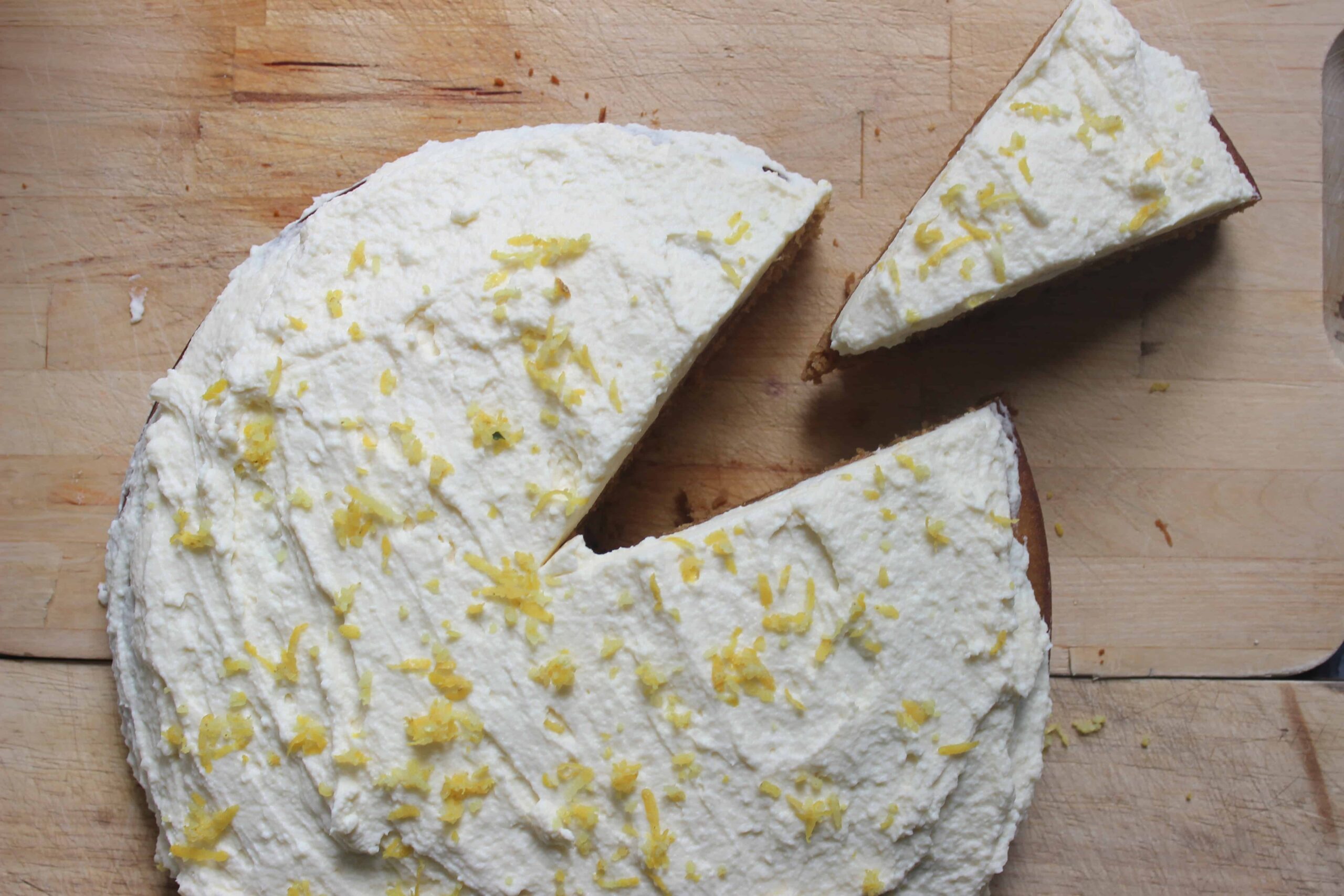 An overhead shot of lemon rosemary cake with olive oil and white frosting on a wooden cutting board.