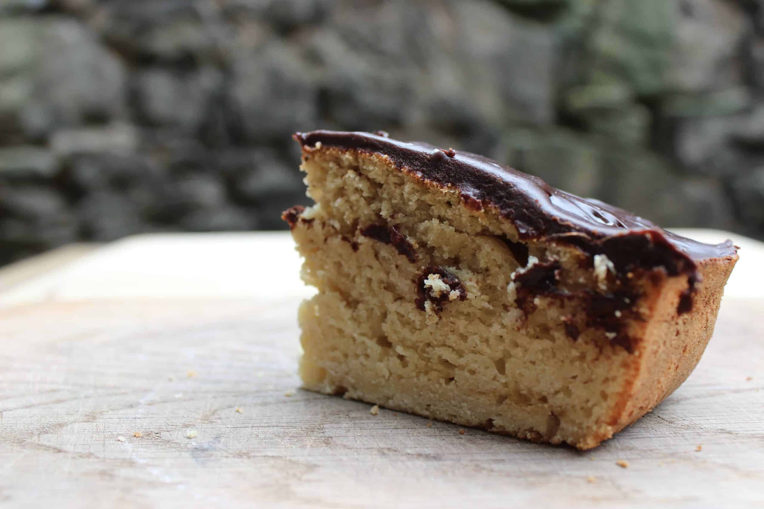 A slice of sourdough vanilla cake with chocolate icing on a wooden cutting board.