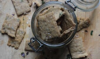An overhead shot of homemade sourdough crackers in a glass mason jar. There is thyme leaves and sea salt sprinkled over top.