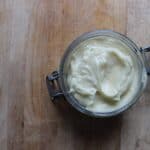 An overhead shot of homemade baby lotion in a glass jar on a wooden cutting board.