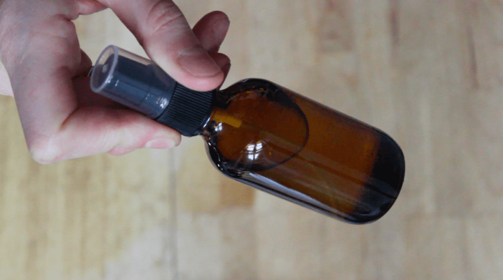 A close up of a small amber glass spray bottle with a wooden cutting board in the background.