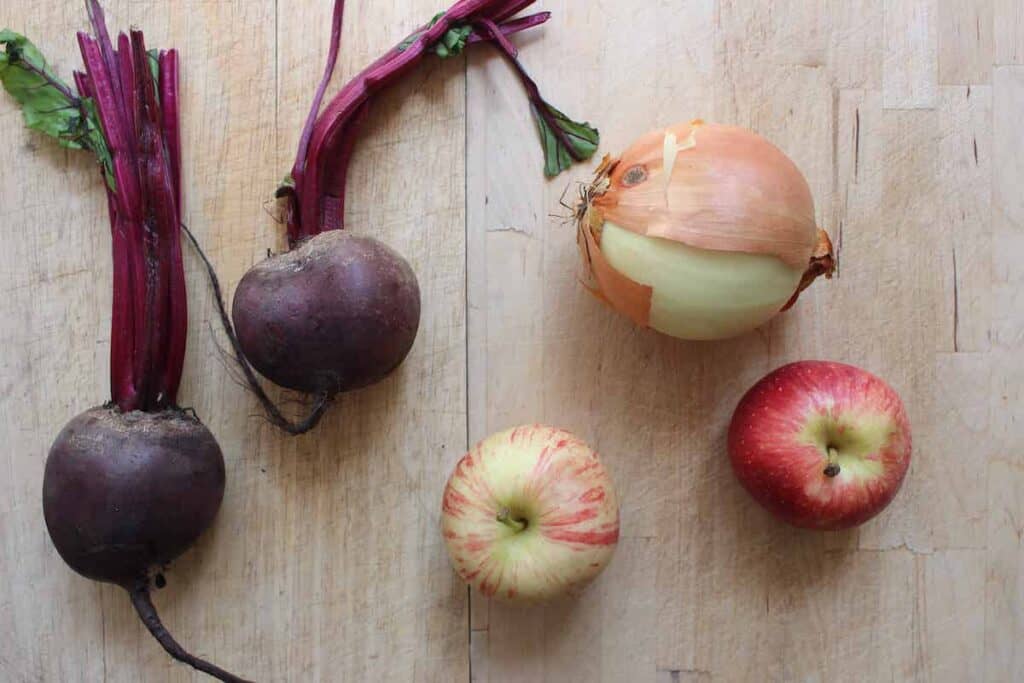 Beetroot, onions, and apples on a wooden cutting board.