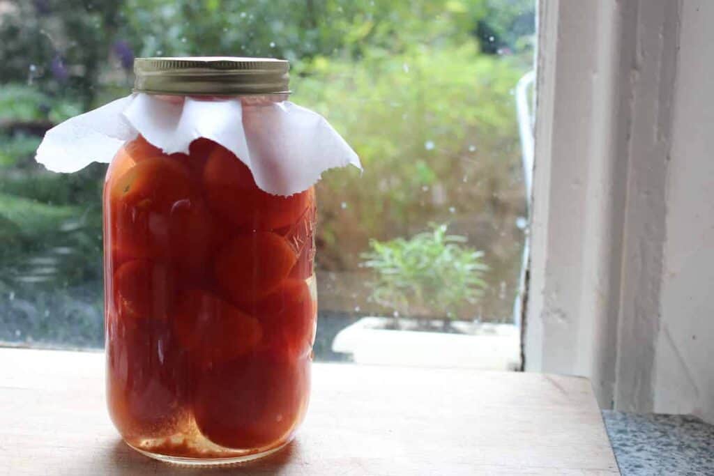 A glass jar of fermenting tomatoes on a wooden cutting board.