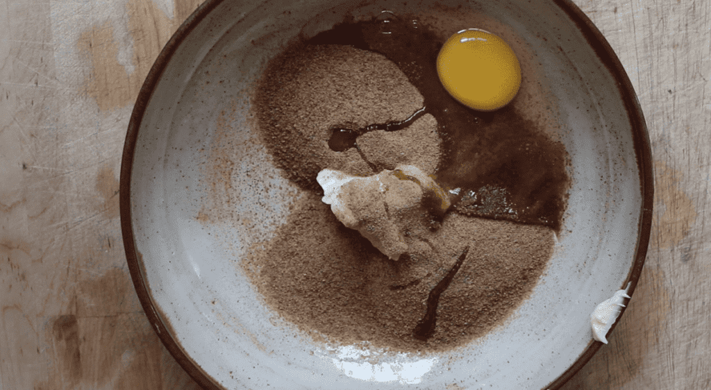 Coconut sugar, an egg, and butter in a pottery bowl on a wooden cutting board.