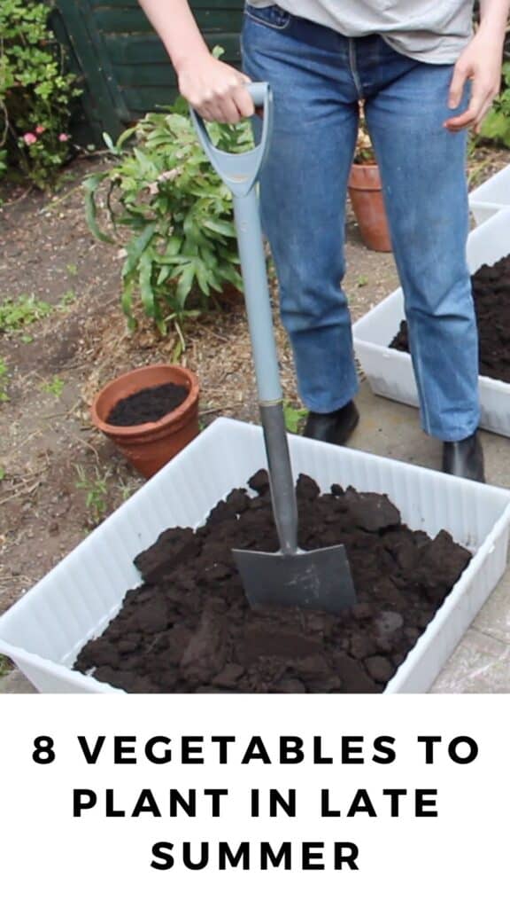 A person using a shovel to break apart soil in a white plastic raised garden bed.