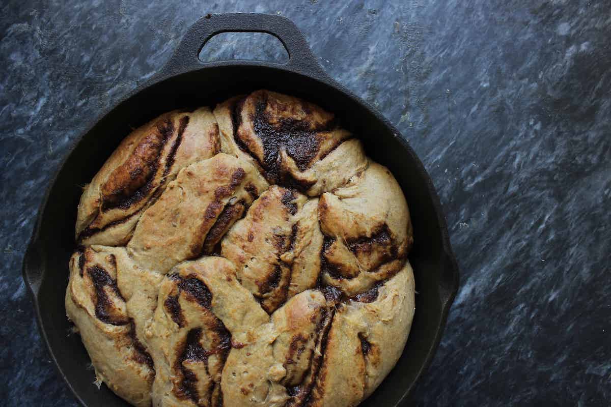 An overhead shot of baked sourdough pumpkin cinnamon rolls in a cast iron skillet on a dark countertop.