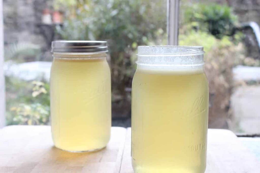 Two mason glass jars of homemade bone broth in front of a window.