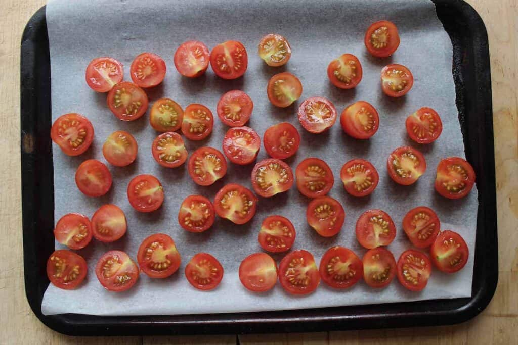 An overhead shot of cherry tomatoes on a baking tray with parchment paper.
