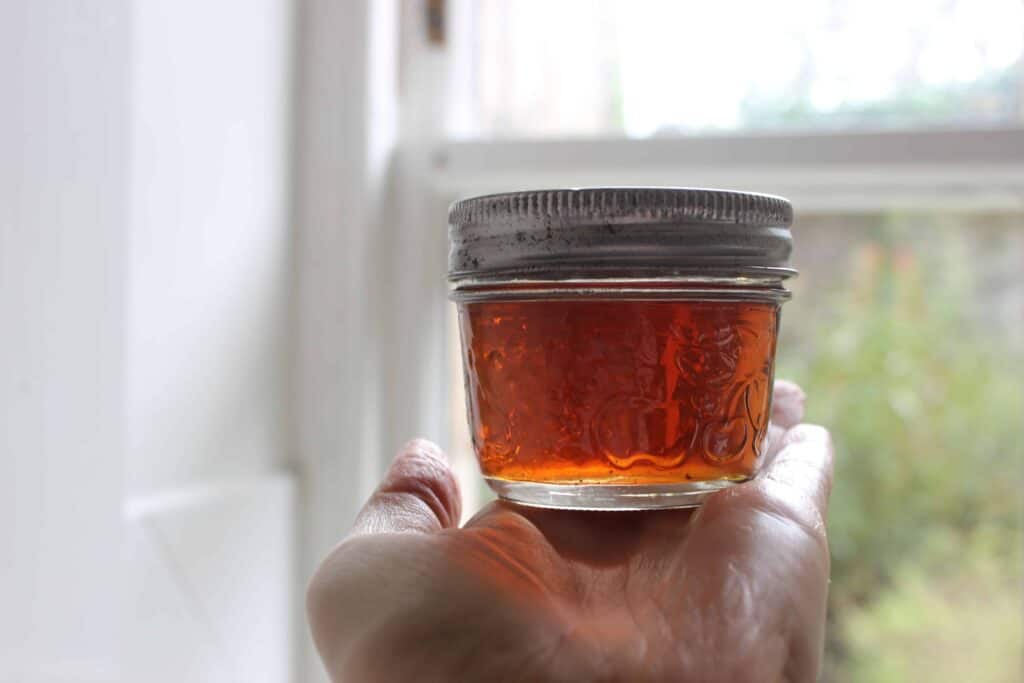 A person holding a small glass jar of elderflower tincture