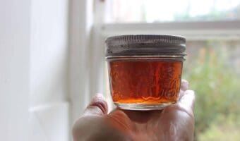 A person holding a small glass jar of elderflower tincture