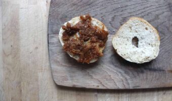 An overhead shot of a bagel cut in half with homemade fig jam on one side. They are lying on a wooden cutting board.