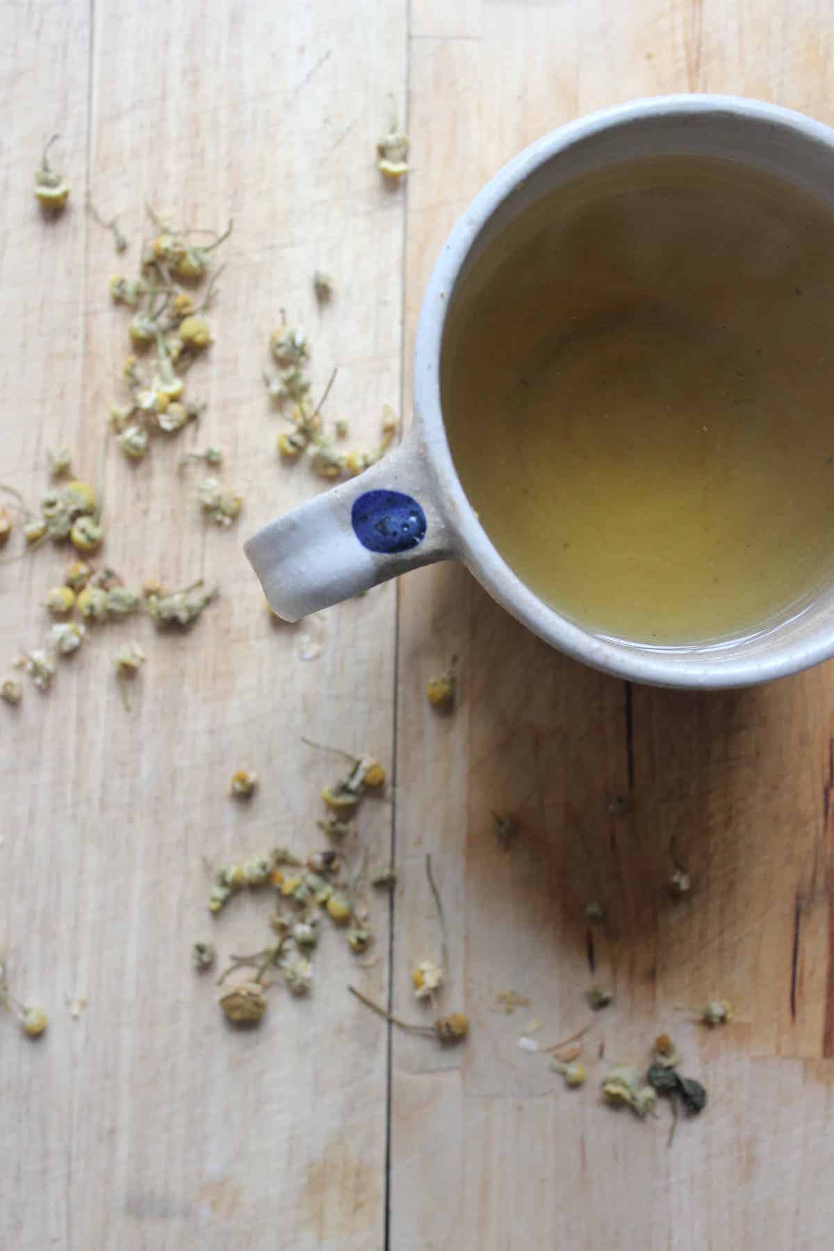A mug of chamomile tea next to dried chamomile flowers on a wooden cutting board.