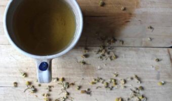 A mug of chamomile tea next to dried chamomile flowers on a wooden cutting board.