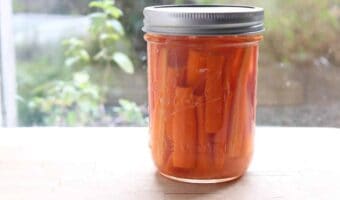 A glass jar on a windowsill with lacto-fermented carrots.