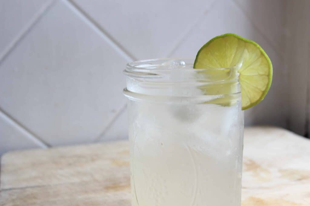 A lemon lime and bitters drink on a wooden countertop with a slice of lime.