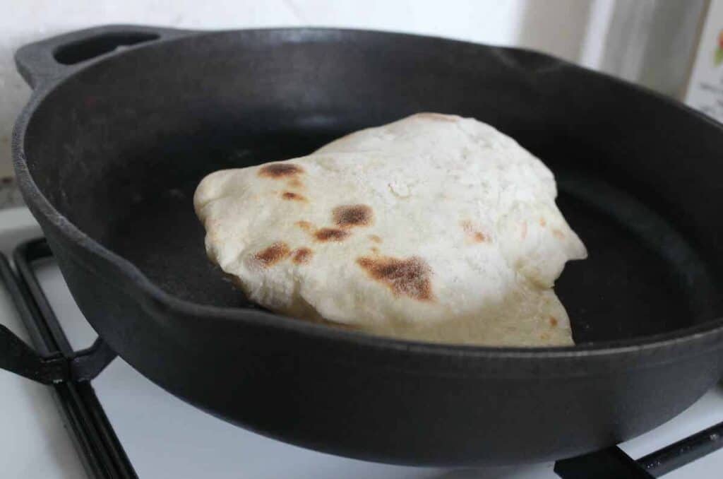 A puffy sourdough discard naan in a cast iron skillet.