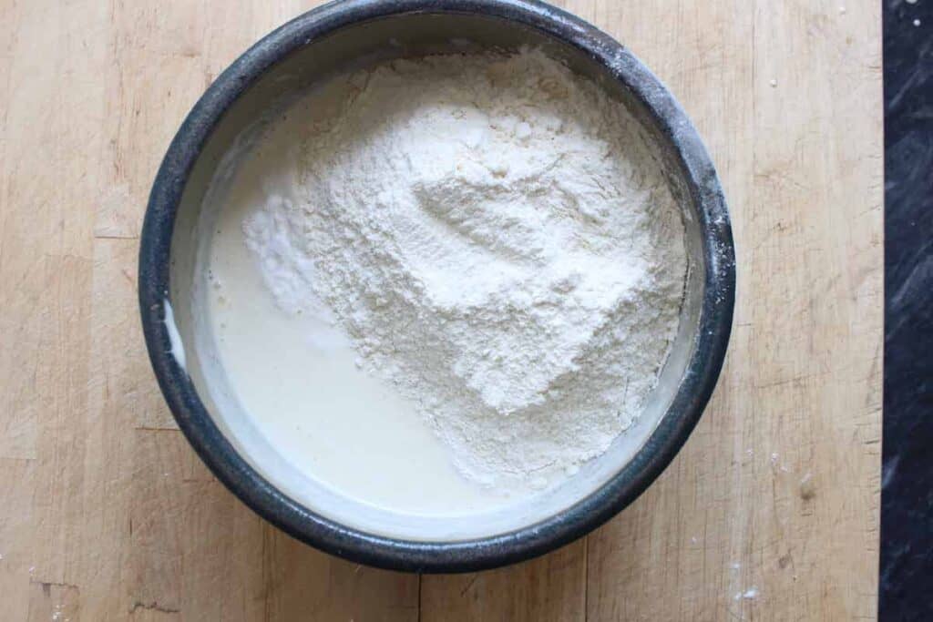 An overhead shot of flour in a pottery bowl. The bowl is on a wooden cutting board.