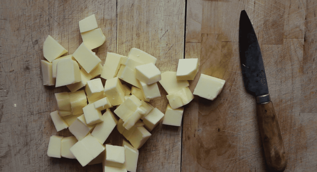 An overhead shot of cubed butter on a wooden countertop. There is a knife beside the butter.