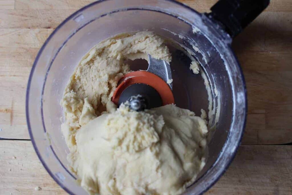 An overhead shot of a food processor on a wooden countertop. There is pie dough in the food processor.