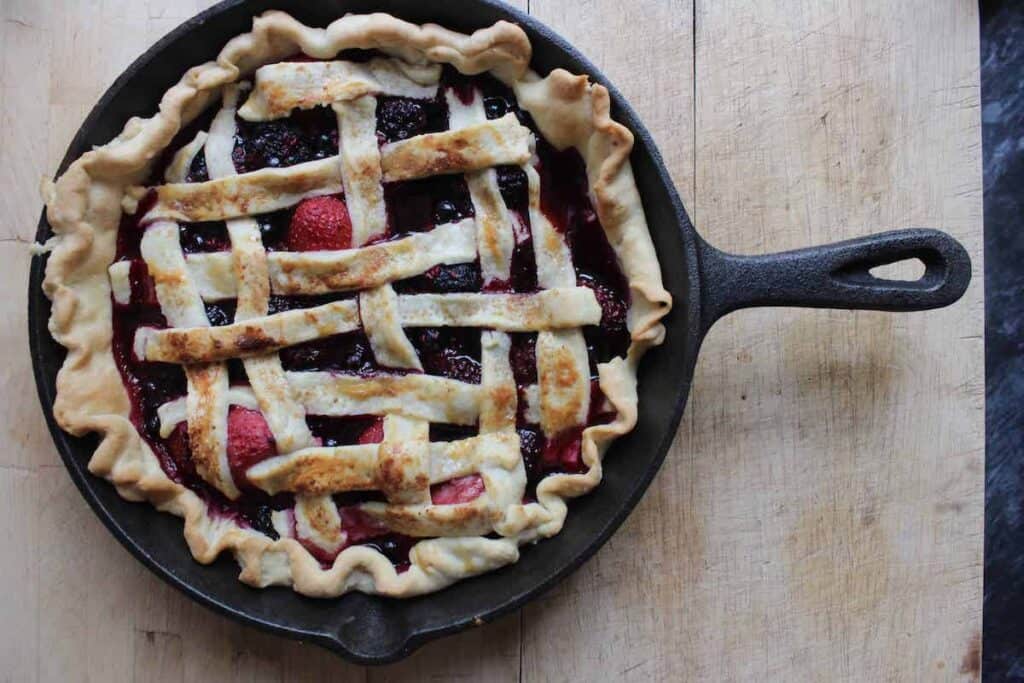 An overhead shot of a baked berry pie on a wooden countertop.