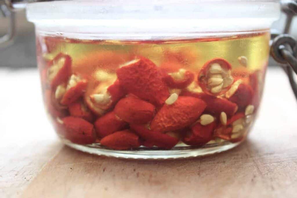 A close up shot of red rosehips infusing in oil. They are in a small glass jar.