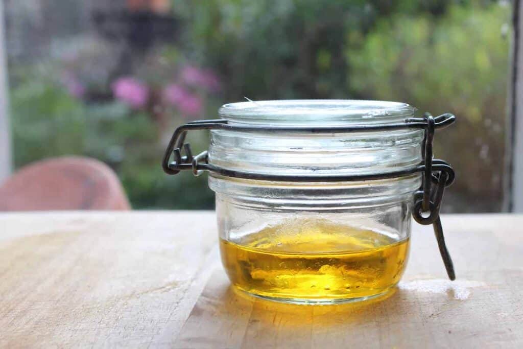A shot of diy rosehip oil in a small glass jar on a light countertop in front of a window.