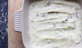 An overhead shot of mashed potatoes with brie in a cream baking dish.