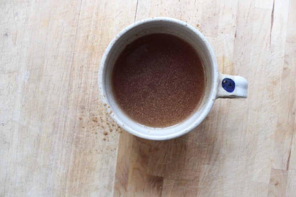 An overhead shot of cacao nib tea in a cream pottery mug on a light countertop.