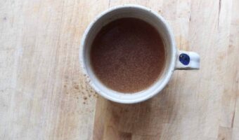 An overhead shot of cacao nib tea in a cream pottery mug on a light countertop.