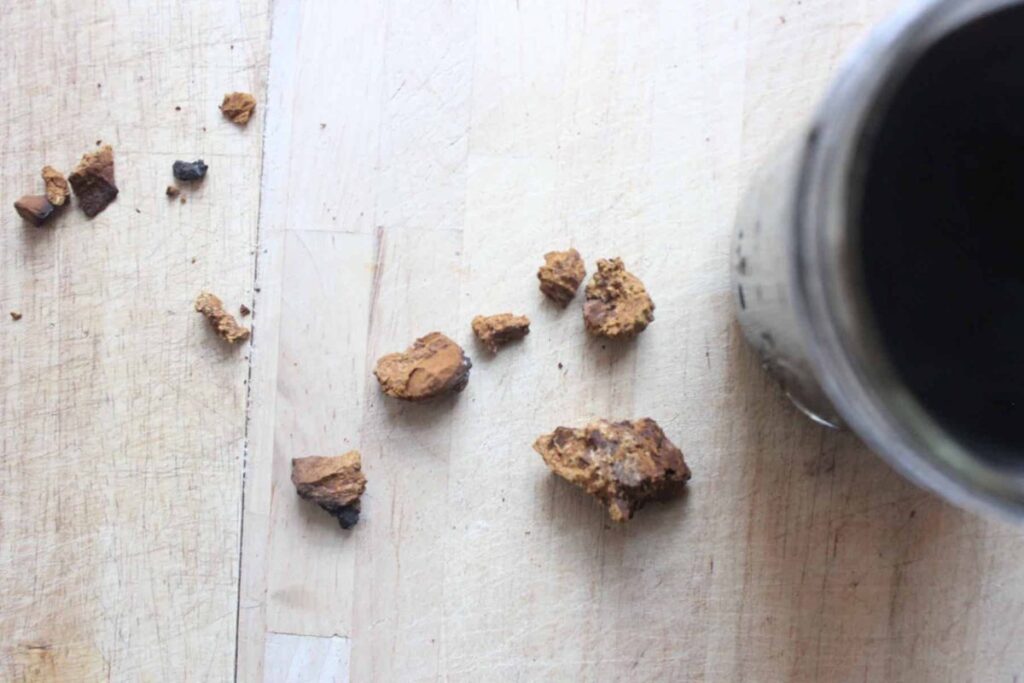 An overhead shot of chaga mushroom chunks on a light countertop next to a jar of chaga tea.