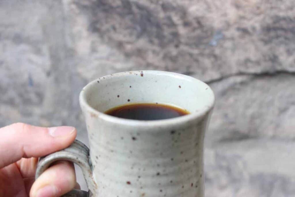 Close up shot of a mug of chaga tea in front of a stone wall.