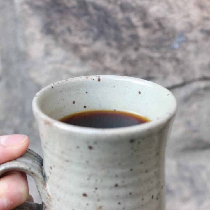 Close up shot of a mug of chaga tea in front of a stone wall.
