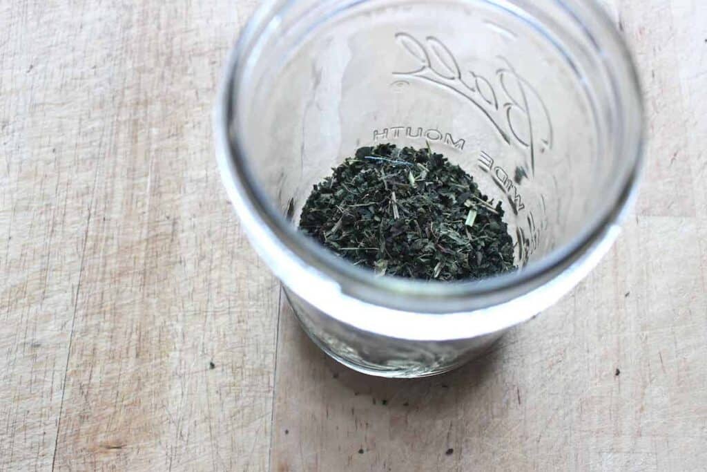 A glass jar with dried nettles on a light countertop.