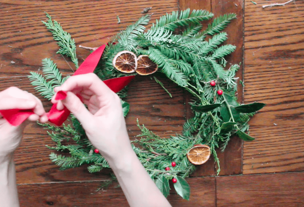 An overhead shot of a person pulling a red ribbon through a homemage foraged wreath.