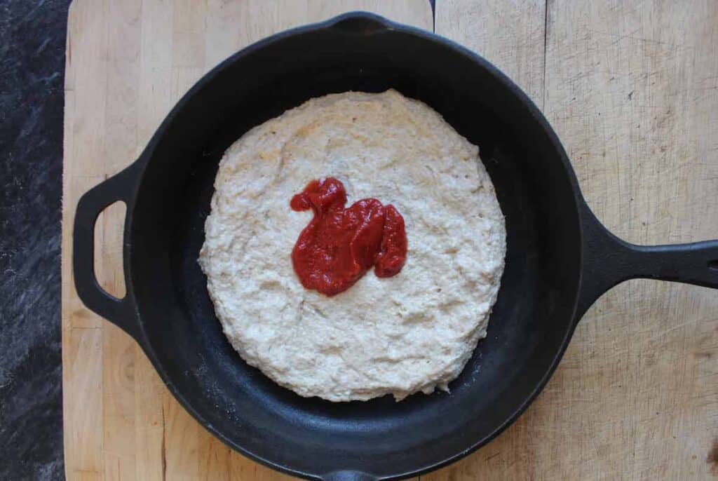 An overhead shot of kamut pizza dough in a cast iron skillet with a dollop of tomato sauce.