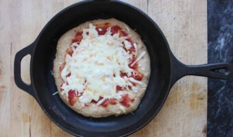 An overhead shot of a baked kamut pizza with cheese and tomato sauce in a cast iron skillet.