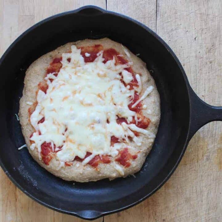 An overhead shot of a baked kamut pizza with cheese and tomato sauce in a cast iron skillet.