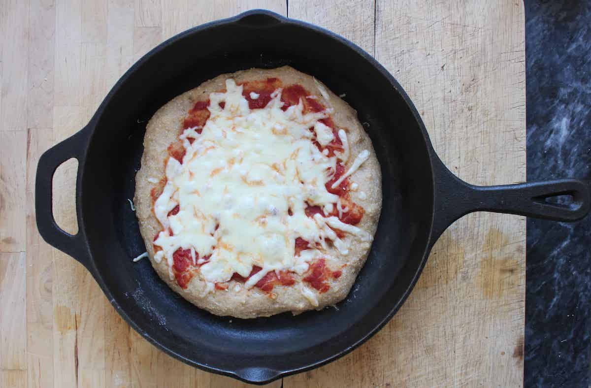 An overhead shot of a baked kamut pizza with cheese and tomato sauce in a cast iron skillet.