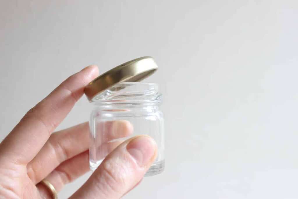 A hand holding a small glass jar.