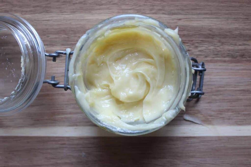 An overhead shot of ﻿﻿beeswax, coconut oil, shea butter, and cocoa butter whipped into a body butter in a glass jar on a light countertop.