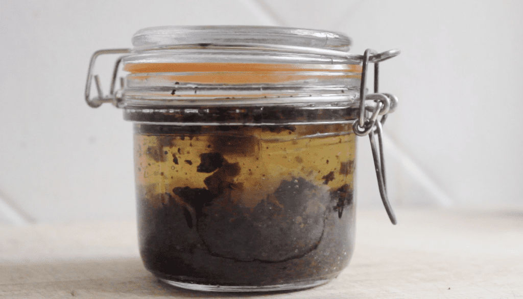 A small glass jar with ground chaga and vodka on a light countertop.