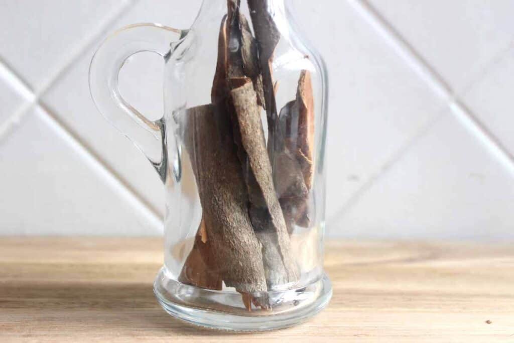 A close up of cinnamon sticks in a glass jar on a light countertop.