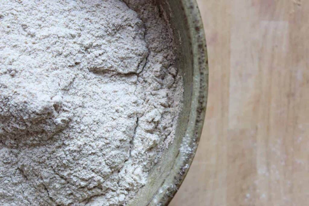 An overhead shot of flour in a green pottery bowl on a light countertop.