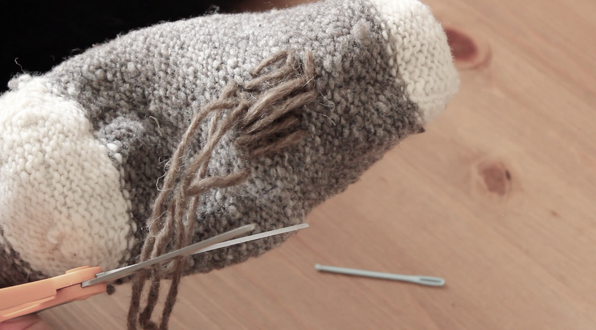 A close up of a person darning a wool sock.
