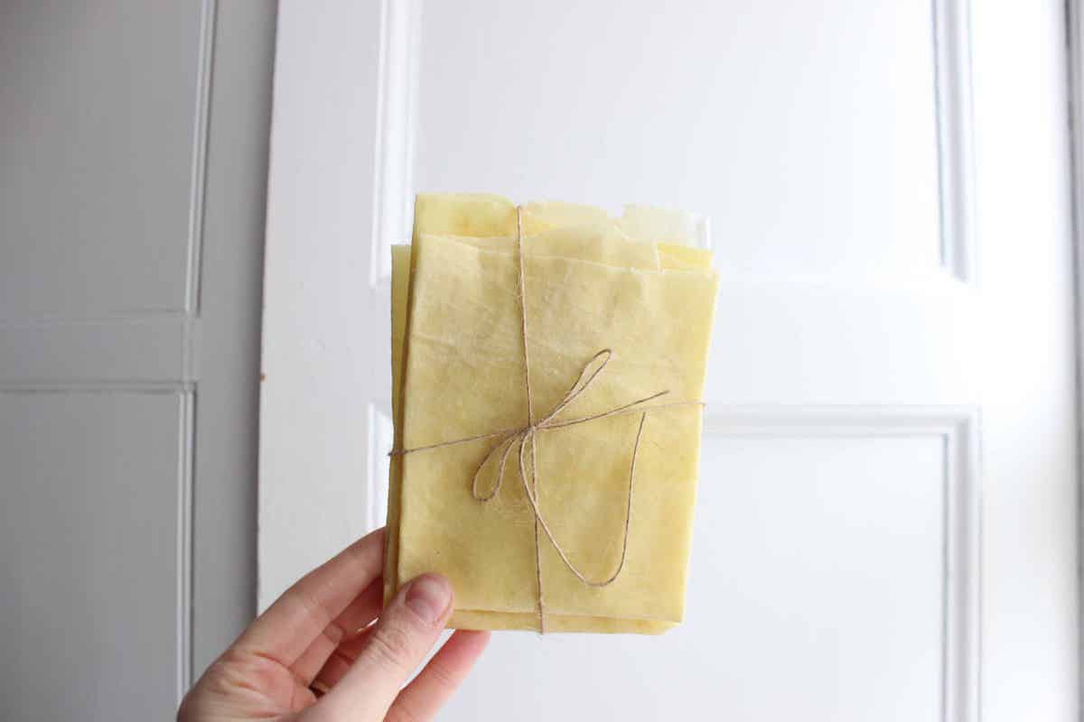 A hand holding a set of yellow homemade beeswax wraps tied in twine.