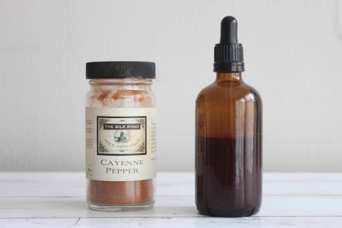 An amber glass dropper bottle with cayenne pepper tincture next to a small glass jar with cayenne pepper in it.